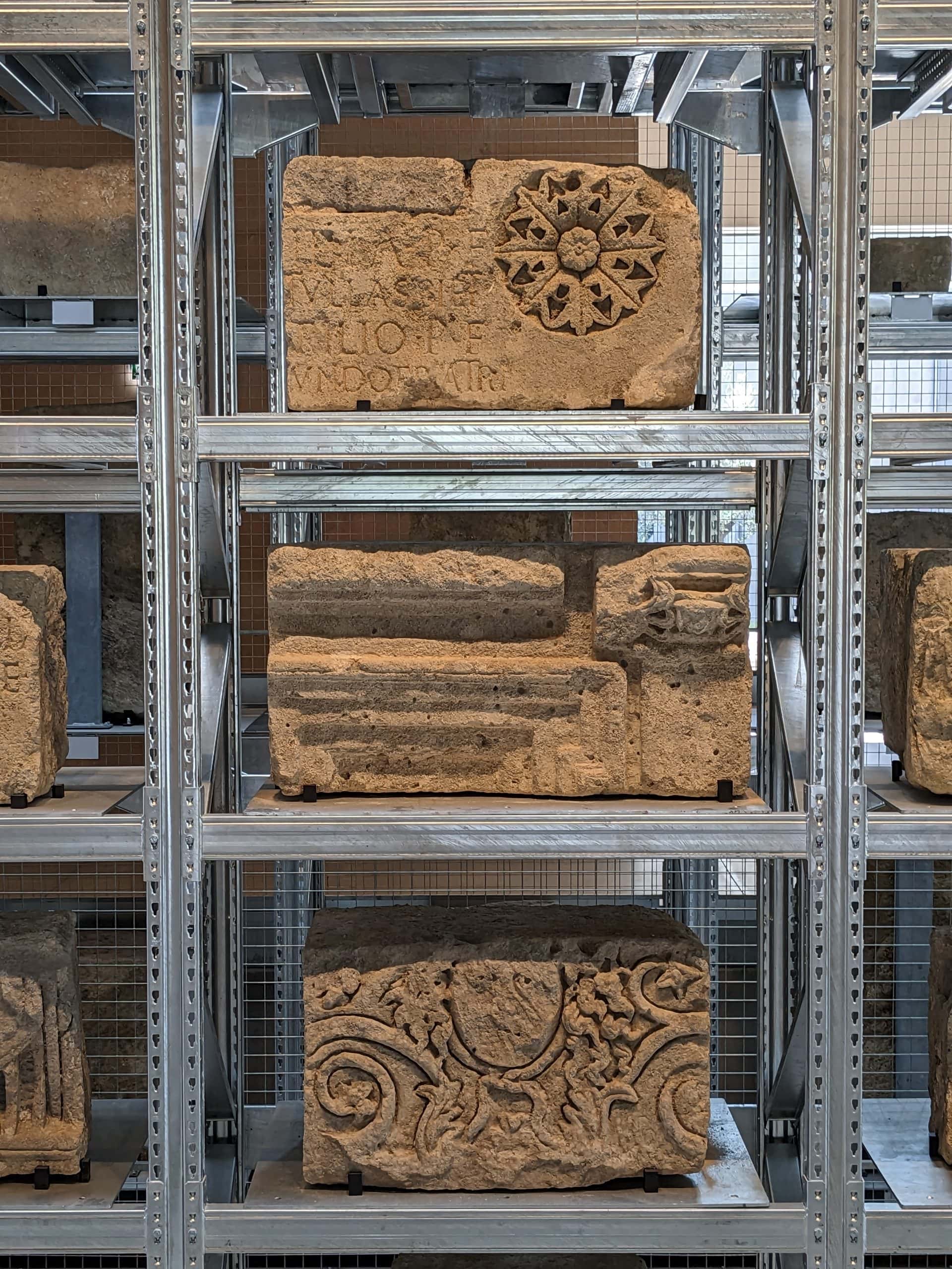A close-up of the "lapidary wall" at Narbo Via, comprising many carved stones held on metal shelves.